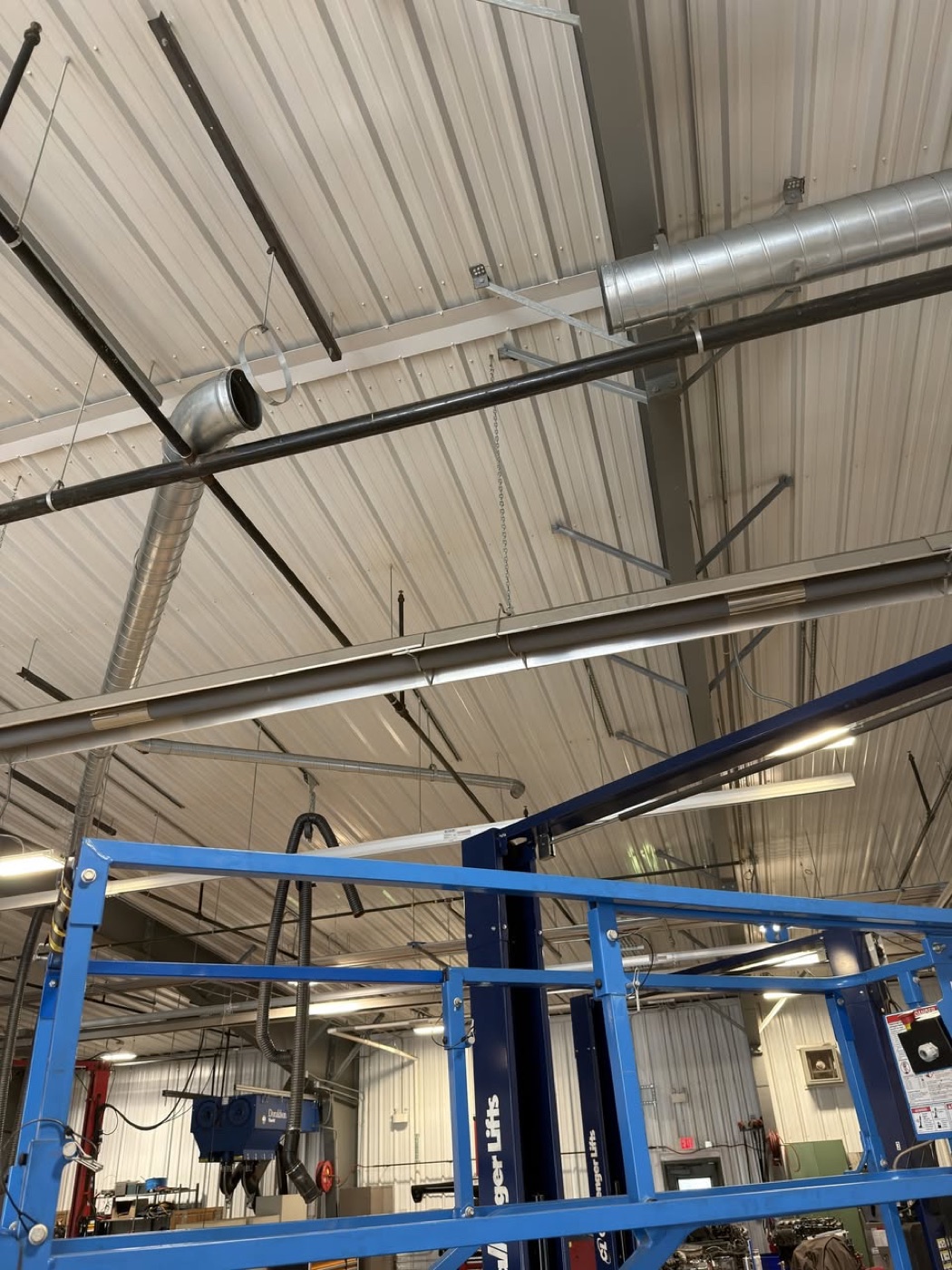 Service shop interior with blue two-post lifts and overhead exhaust extraction ducting